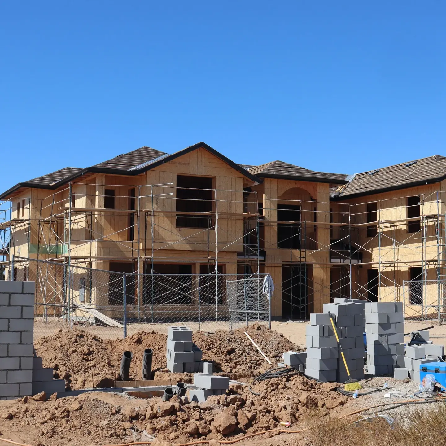 Façade d’une maison individuelle en travaux d’isolation par l’extérieur : échafaudage monté devant le mur et matériaux de chantier au sol.